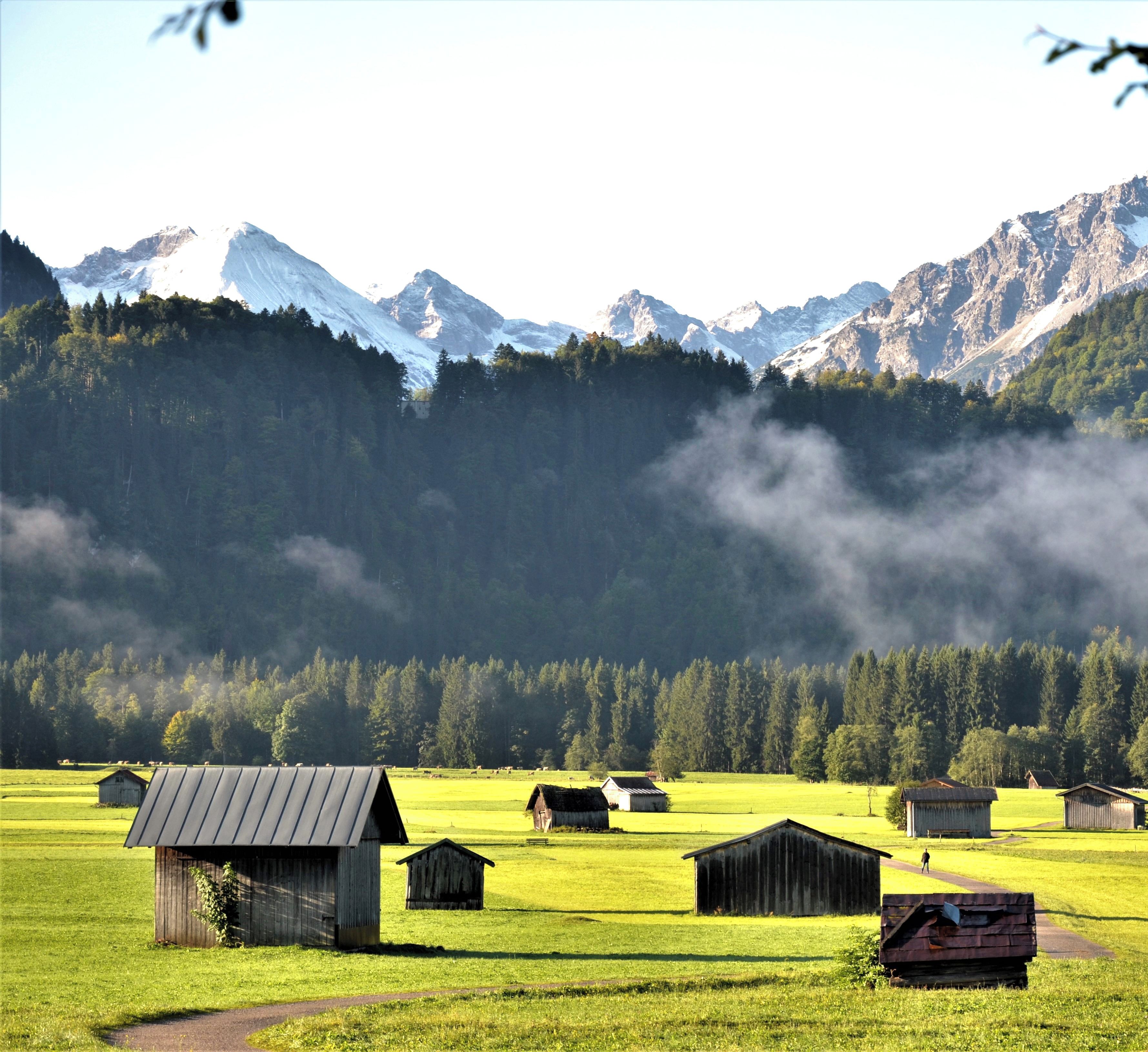 Paisaje rural con una cadena montañosa al fondo, cielo despejado y varias pequeñas construcciones de madera.