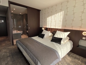 Moderni hotellihuone, jossa on suuri sänky, suihkutila ja näkymä kaupungin ylle.