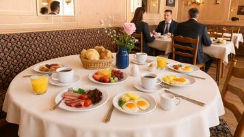 Ein Frühstücksbuffet mit verschiedenen Speisen, darunter Eier, Früchte und Gebäck, in einem Raum mit gemustertem Wandpapier und Holzmöbeln.