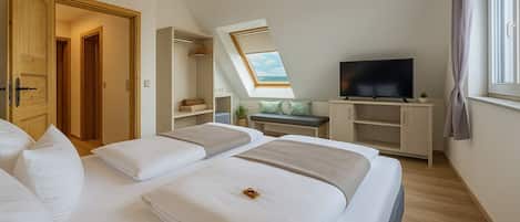 A bedroom with two beds, a TV, a desk, and a window with a view.