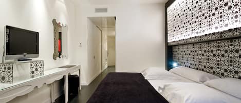 Una habitación de hotel moderna con cama, escritorio con televisor de pantalla plana, espejo decorativo y cabecera estampada.