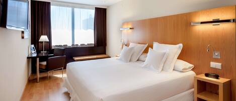 A hotel room with a large bed, a desk, a chair, a TV, and a window with curtains.