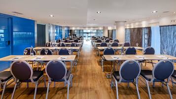 A conference room with rows of tables and chairs, large windows, and a blue accent wall.