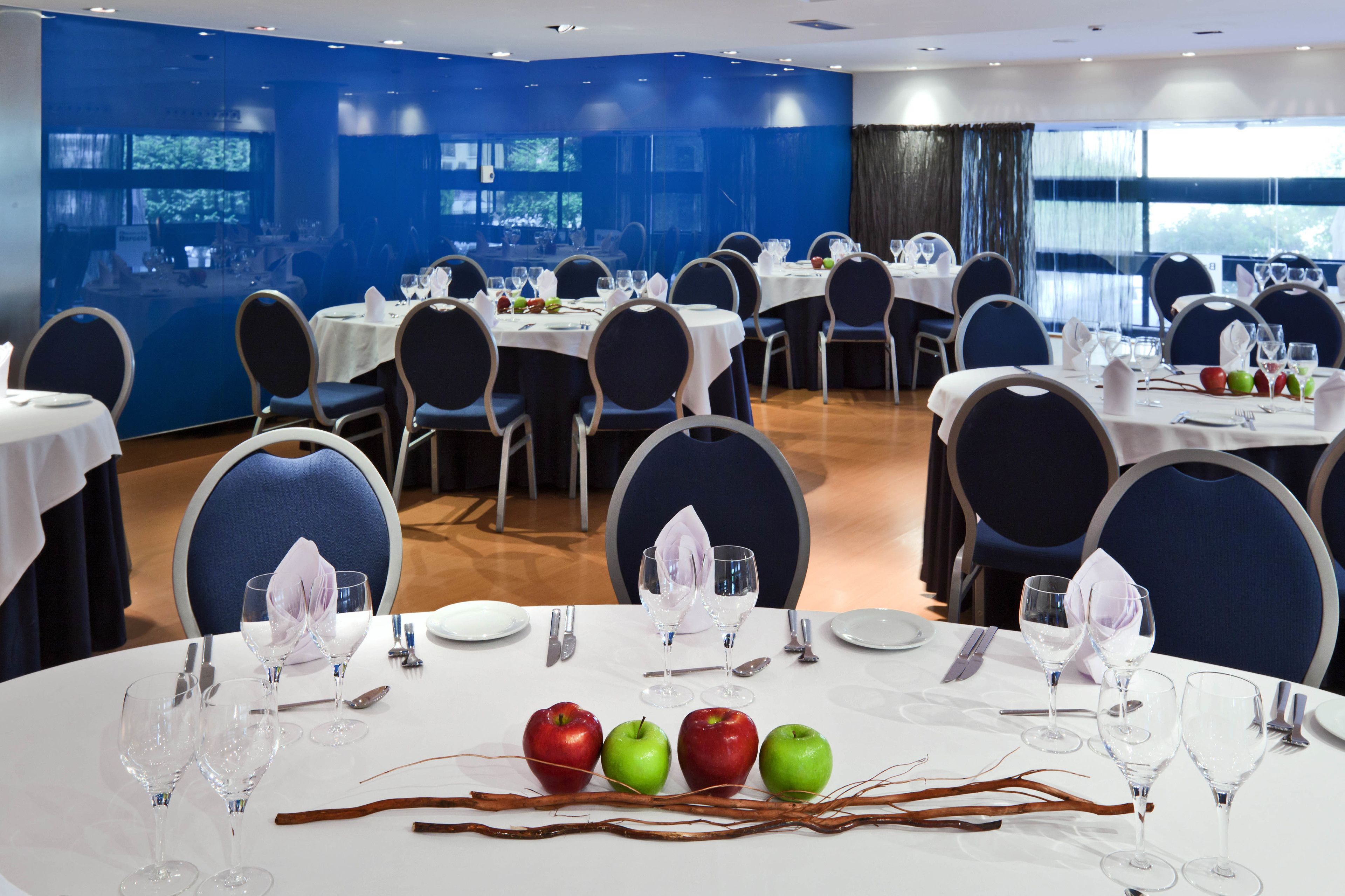 Un comedor con mesas redondas, sillas y mesas dispuestas con platos, cubiertos y copas de vino.