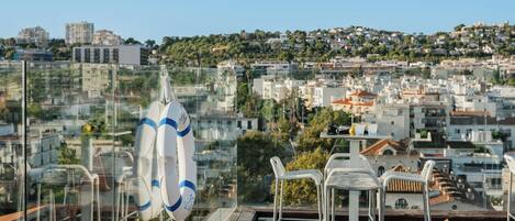 A rooftop terrace with a clear view of a cityscape, including buildings and greenery.