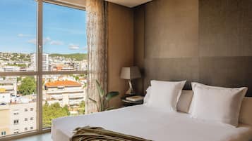 Une chambre d’hôtel avec un grand lit, une table de chevet, une lampe et une vue sur le paysage urbain grâce à de grandes fenêtres.
