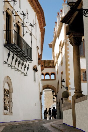 A narrow street with white buildings, arched doorways, and black wrought iron balconies. - MIM Sitges Member of Meliá Collection (Sitges)