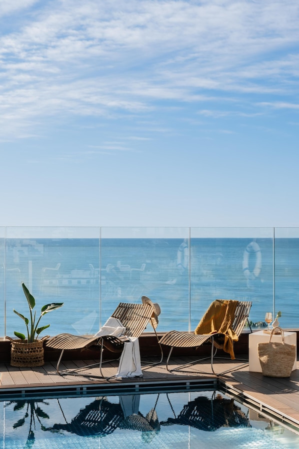 A poolside area with lounge chairs and a clear view of the ocean.