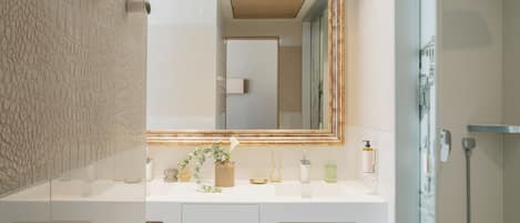 A modern bathroom with a large mirror, white vanity, and a shower area.
