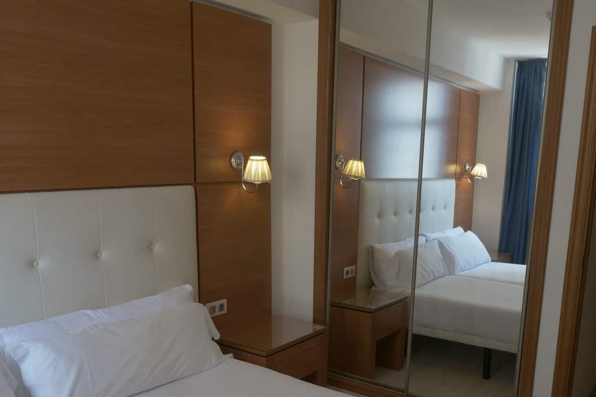 A hotel room with a large bed, a wooden headboard, a nightstand, and a mirror with a wooden frame.