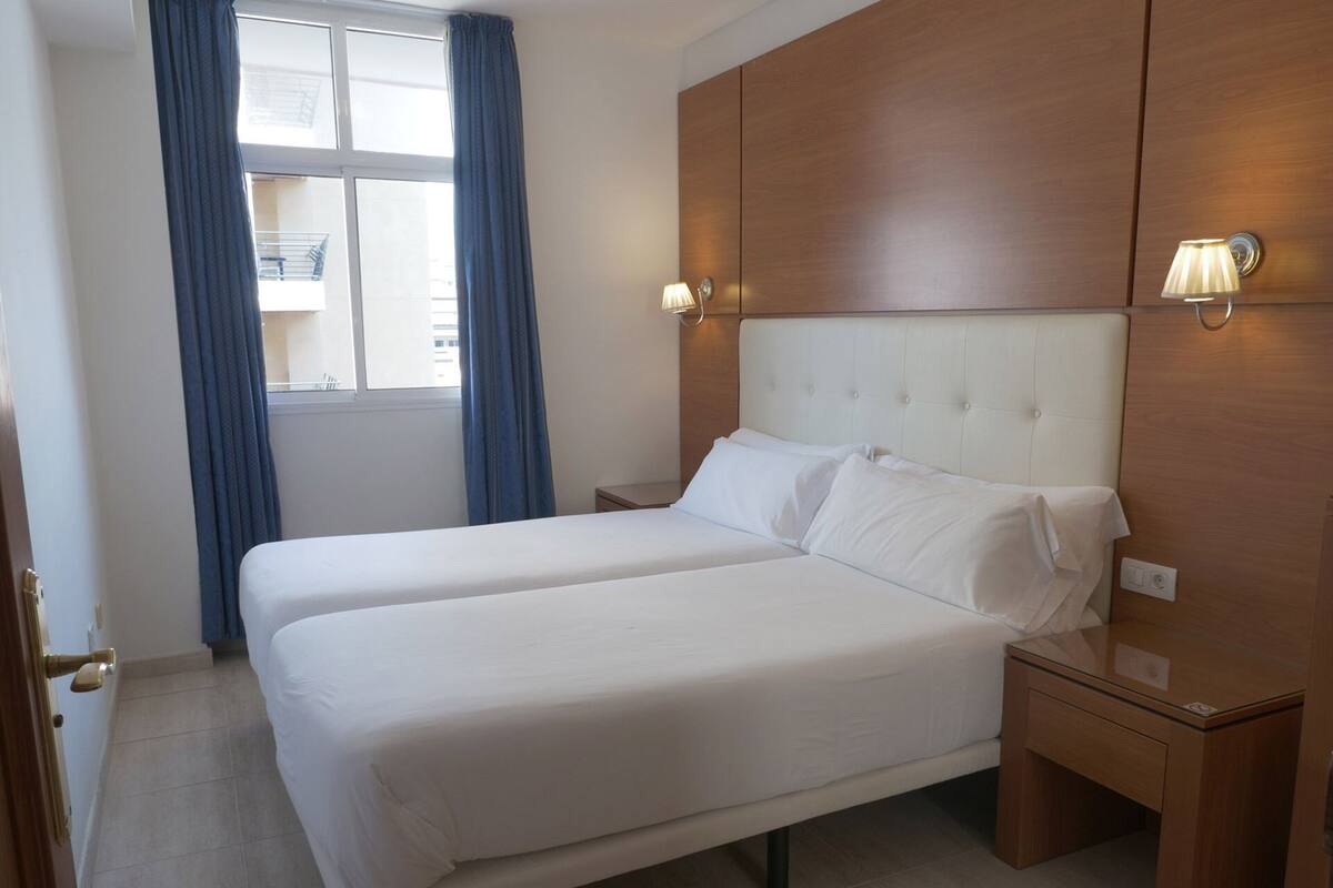 A hotel room with a double bed, two bedside tables, a wooden wardrobe, and a window with curtains.