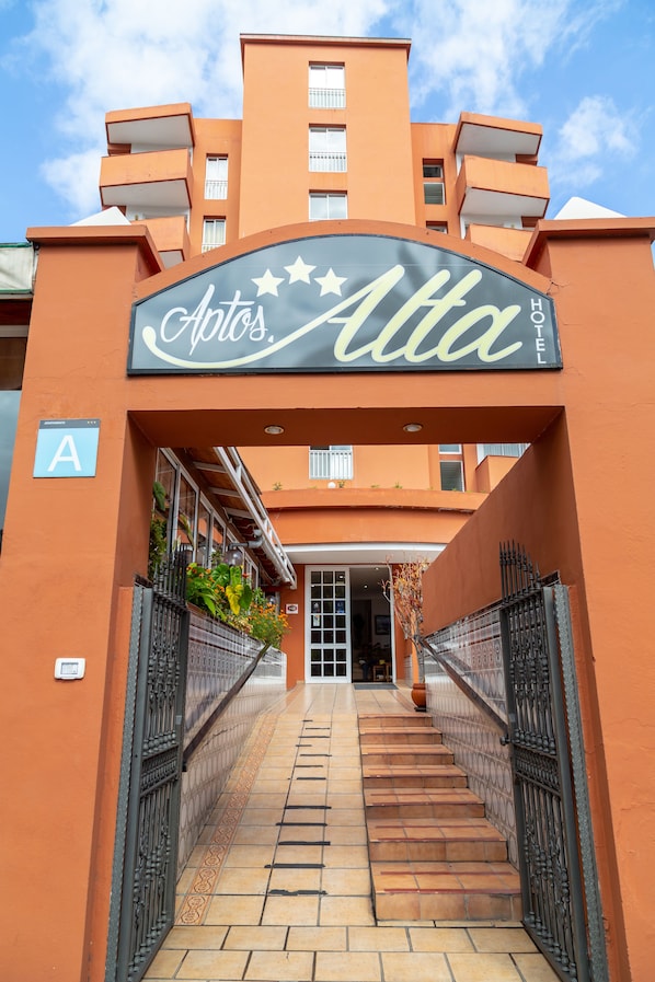 The entrance to a hotel named "Apta Hotel" with a sign above the door, a staircase leading up to the entrance, and a gated pathway on either side.