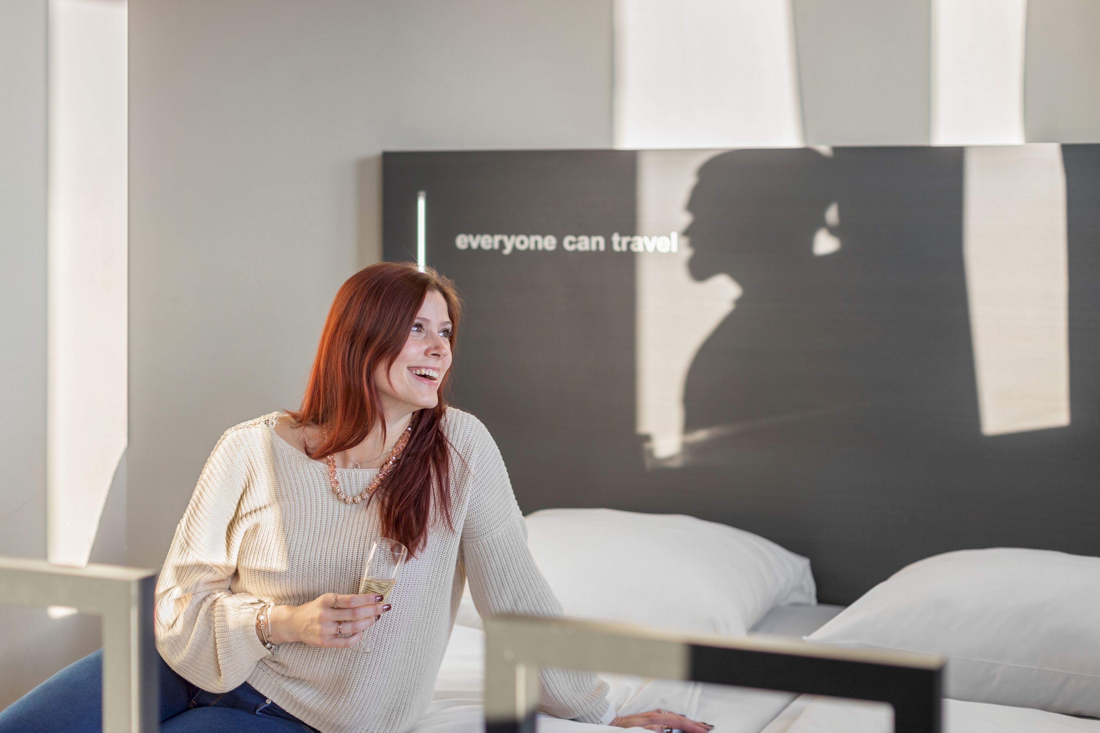 A person sitting on a bed in a room with a large poster on the wall that reads "everyone can travel."