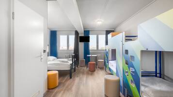 Une chambre d’hôtel moderne avec des lits superposés, un téléviseur à écran plat, une petite table et une fenêtre donnant sur la ville.