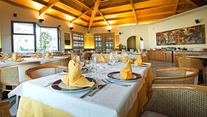 A restaurant with wooden beams, tables set with yellow napkins, and a large painting on the wall. - Hotel President (Correggio)