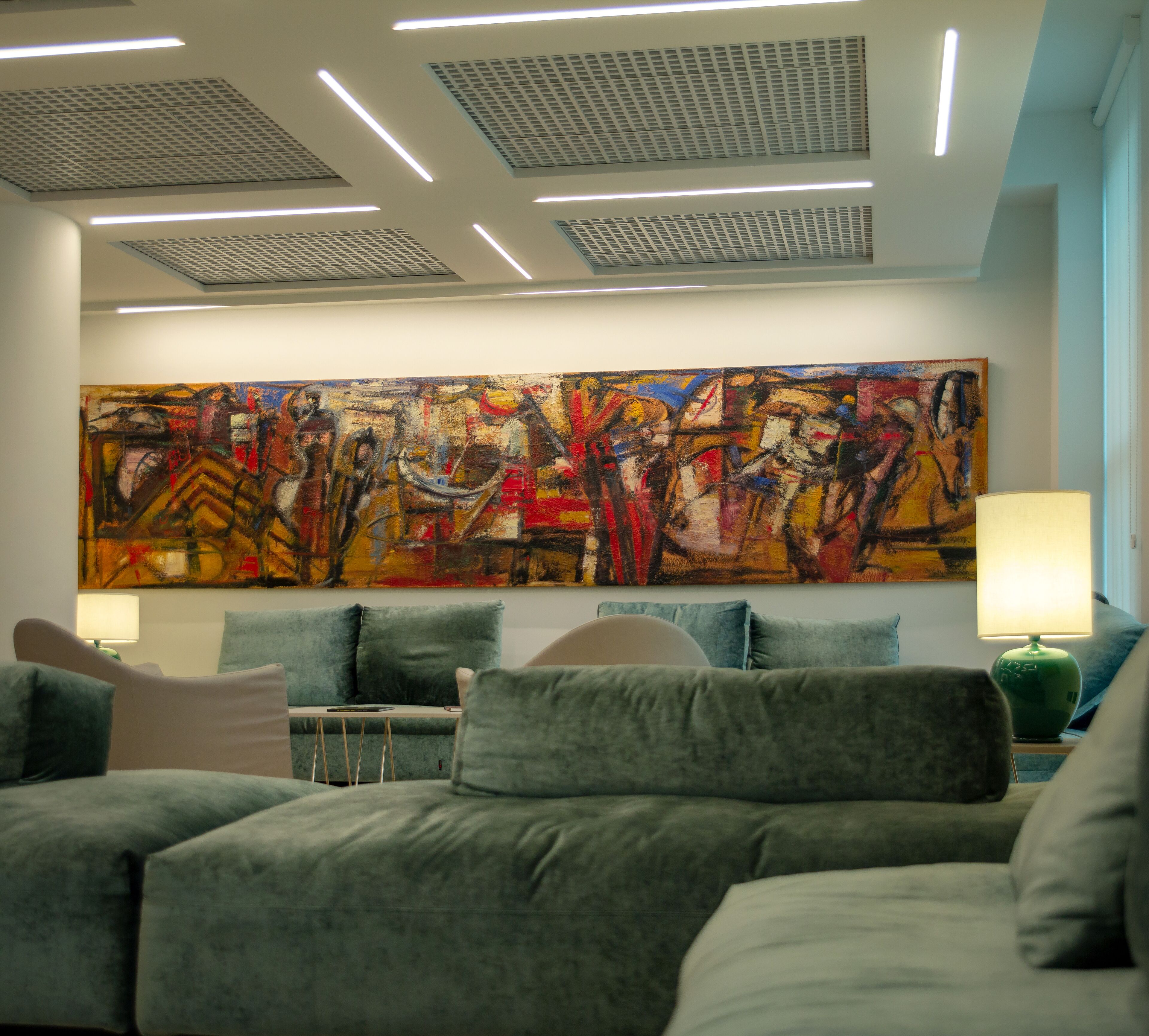 A modern living room with a large abstract painting, grey sofas, and a green lamp.
