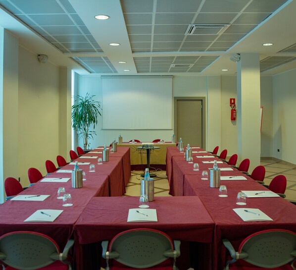 A conference room with a long table, red chairs, a projector screen, and a fire extinguisher. - Hotel President (Correggio)