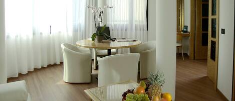 A modern dining area with a round table, white chairs, and a fruit bowl on the table.