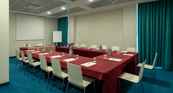 Una sala de conferencias con varias mesas y sillas, una pizarra y una pantalla para proyector.