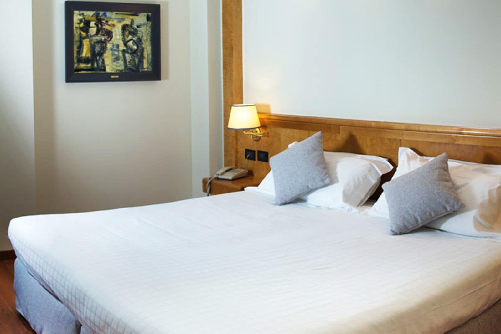 A hotel room with a large bed, a bedside lamp, a phone, and a painting on the wall.