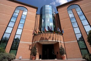 A building with a brick facade, large arched windows, and a central glass tower. - Hotel President (Correggio)