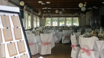 A banquet hall with tables set for a formal event, white tablecloths, and chairs with pink sashes.