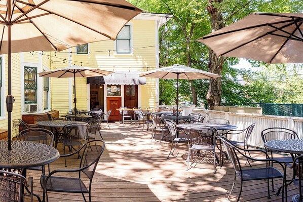 An outdoor patio with tables and chairs, shaded by umbrellas, and a building in the background. - The Charleston Inn (Hendersonville)