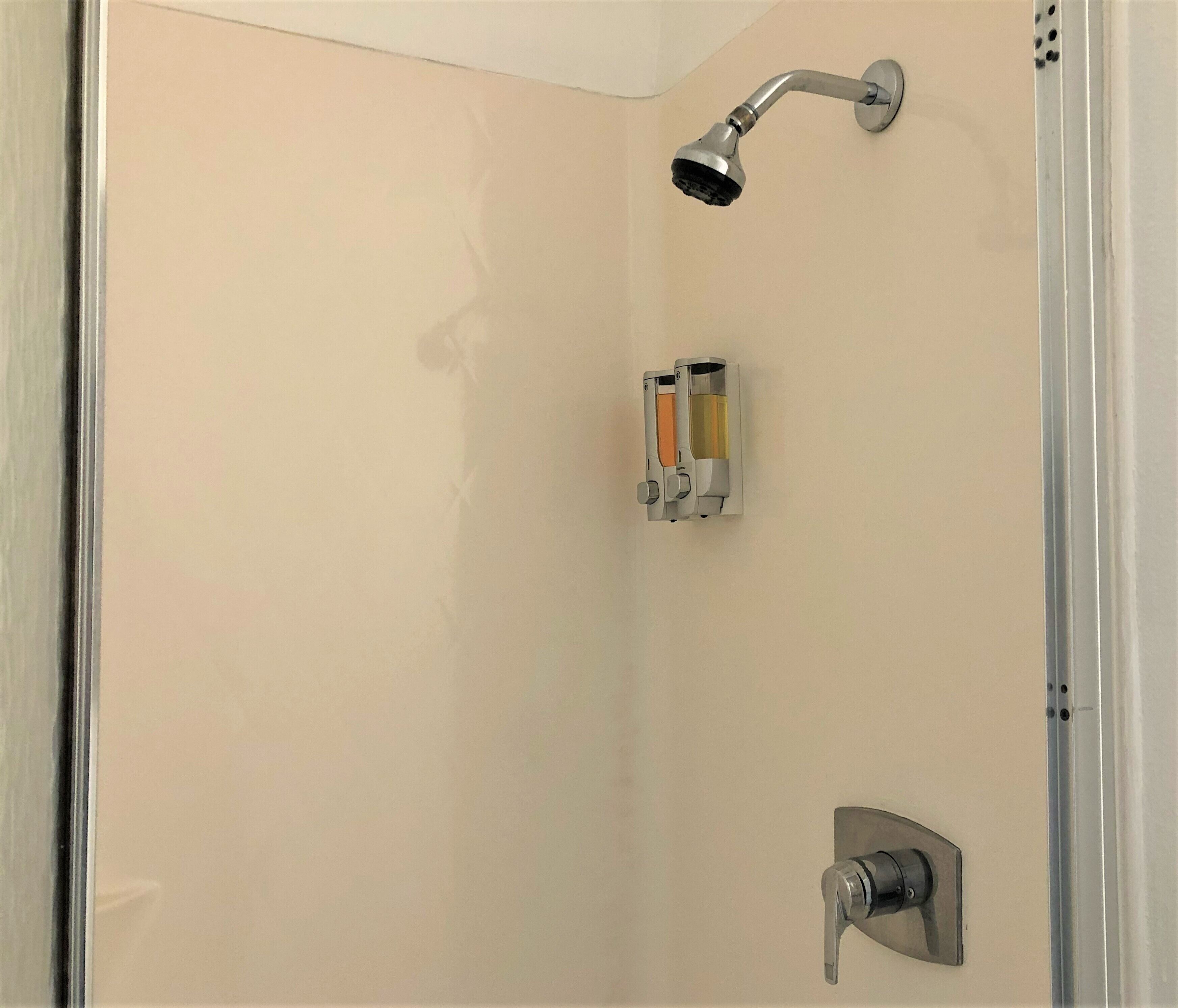Eine Dusche mit Duschbrause, Seifenspender an der Wand und Handtuchhalter.