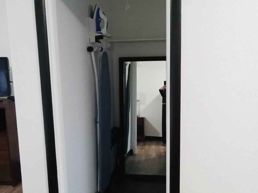 Un pasillo con suelo de madera, marco de puerta blanco y un espejo que refleja a alguien tomando una fotografía.