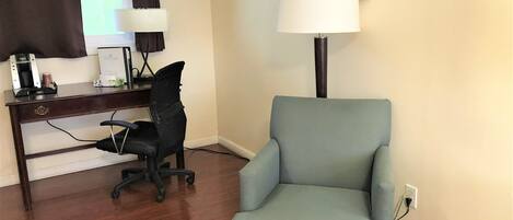 A room with a desk, chair, lamp, and a painting on the wall.