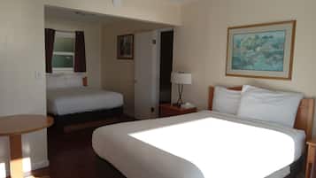 A hotel room with a large bed, a smaller bed, a desk, a lamp, and a painting on the wall.