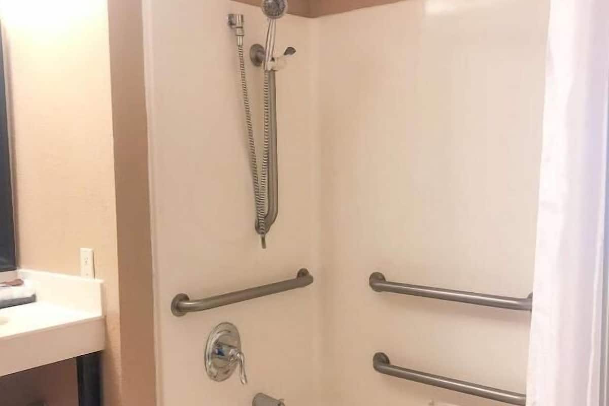 Une salle de bain équipée d’une douche à l’italienne, de barres d’appui, d’un petit marchepied et d’un lavabo.