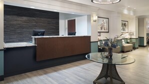 A modern reception area with a dark wood reception desk, a glass table with a vase, and a chandelier. - Best Western Plus Frontier Inn (Cheyenne)
