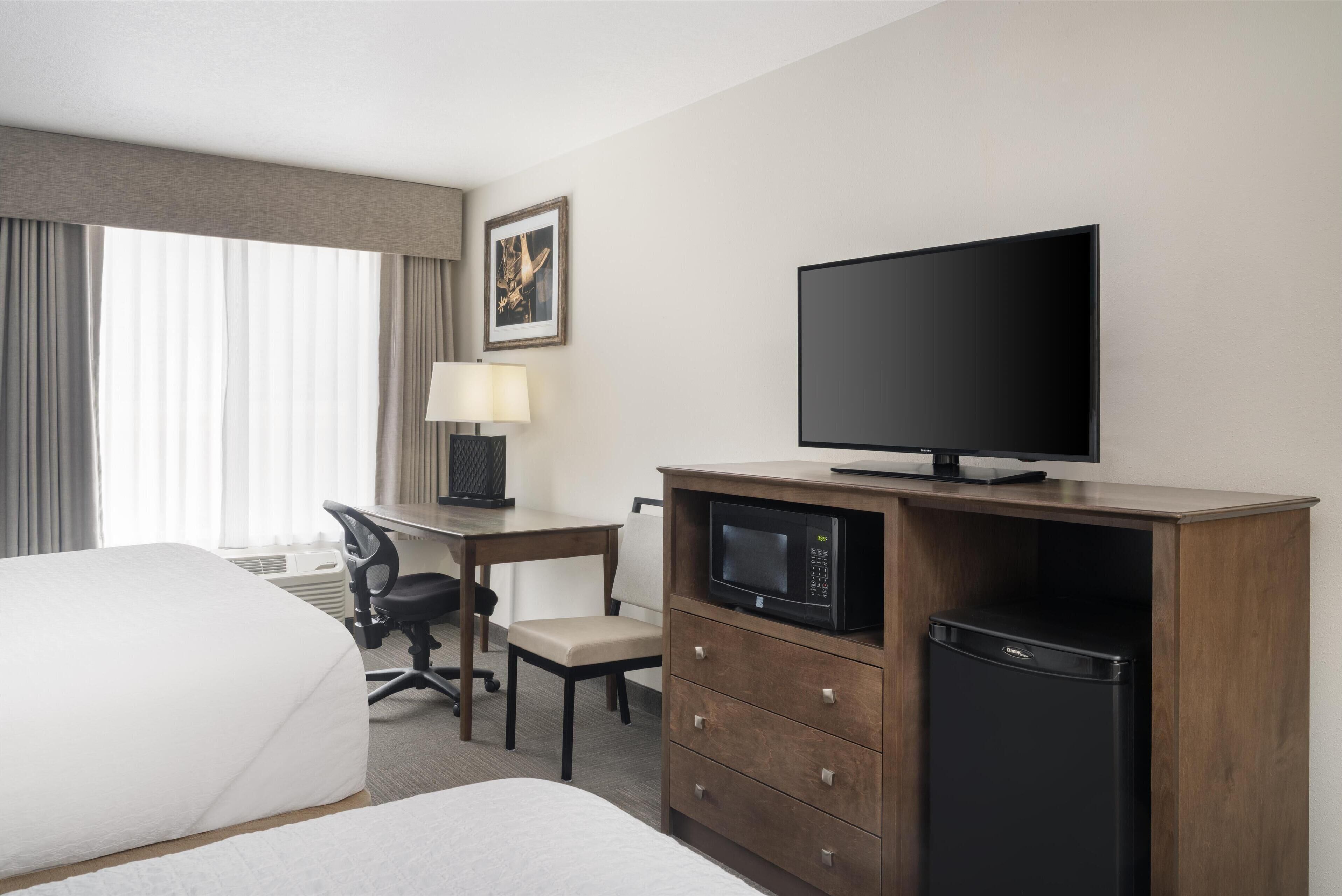 A hotel room with a bed, a desk with a chair, a television, a microwave, and a refrigerator.