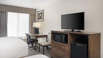 A hotel room with a bed, a desk with a chair, a television, a microwave, and a refrigerator.