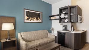 A compact living space with a sofa, a coffee table, a lamp, a kitchen area with a microwave, and a dishwasher. - Best Western Plus Frontier Inn (Cheyenne)