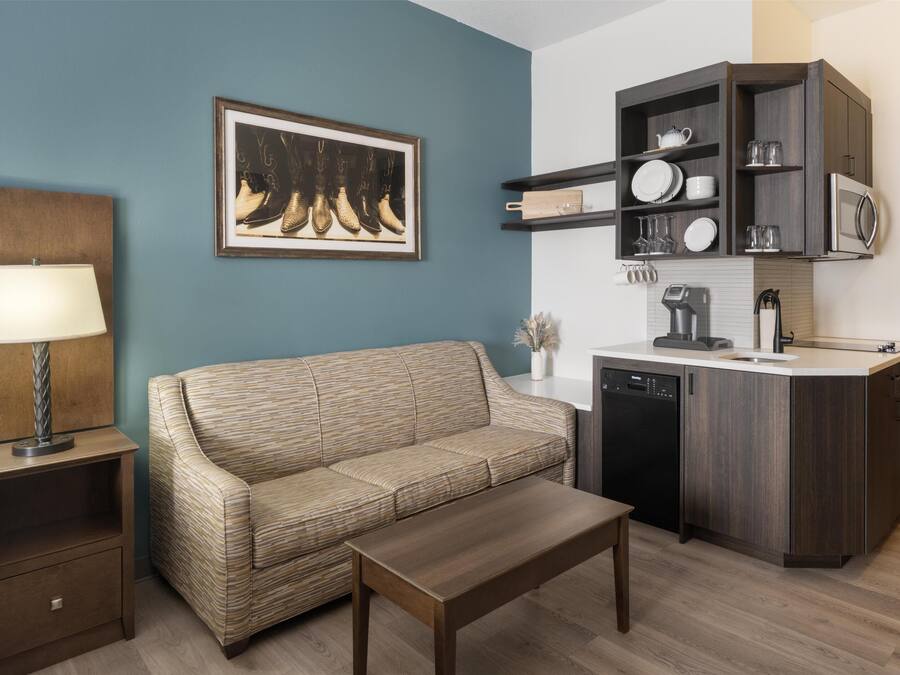 Un espacio habitable compacto con sofá, una mesa de centro, una lámpara, zona de cocina con microondas y lavavajillas.
