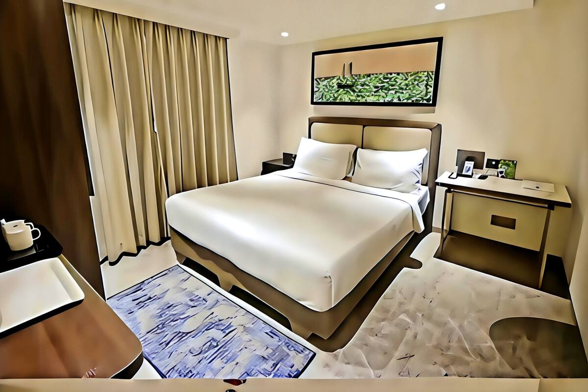 A hotel room with a large bed, bedside table, desk, and a painting on the wall.