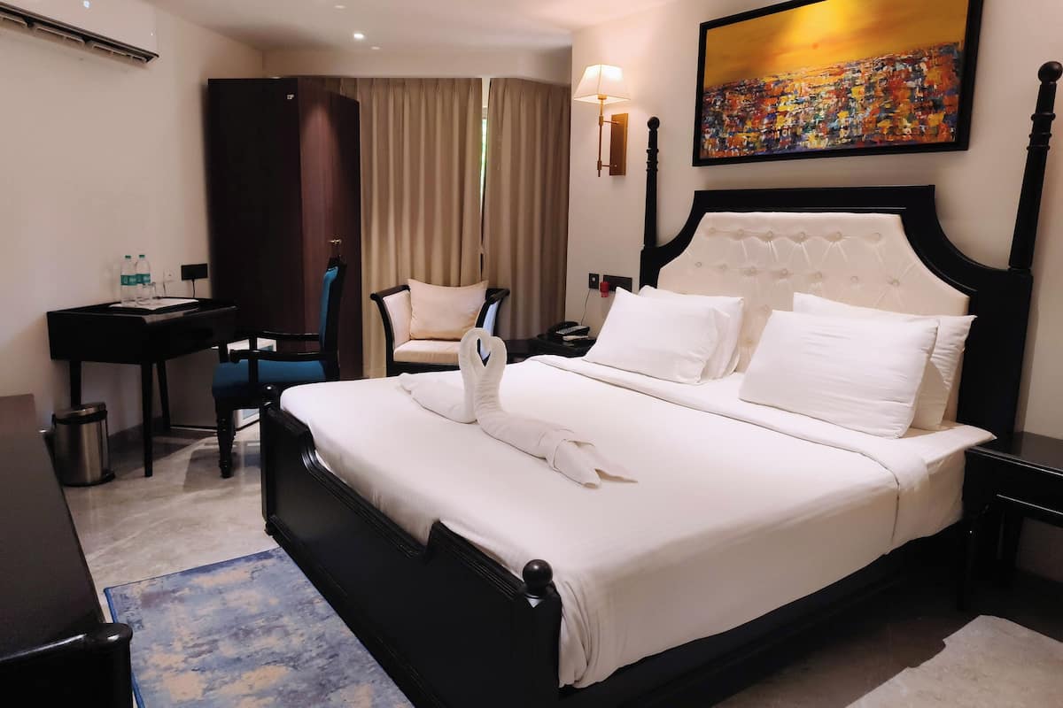 A hotel room with a large bed, a desk, a chair, a bedside table, a lamp, and a painting on the wall.