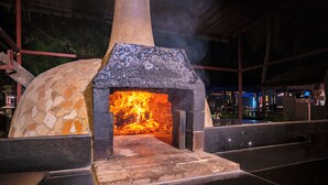Un horno de piedra con fuego encendido en su interior, rodeado de un piso de azulejos y una baranda de metal.