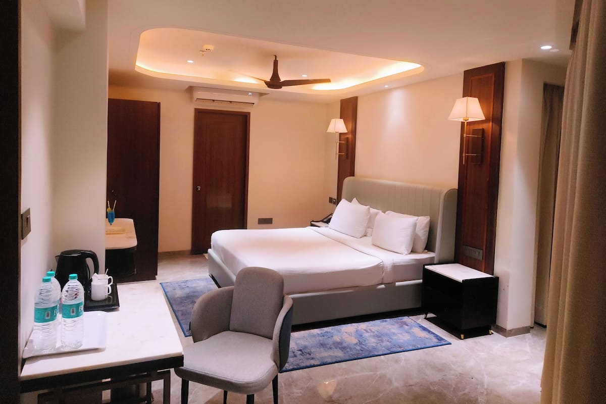 A hotel room with a bed, bedside tables, a desk with a chair, a coffee maker, and a water dispenser.