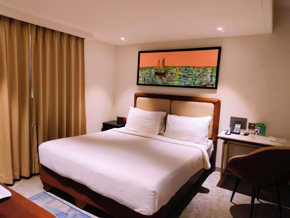 A hotel room with a bed, a desk, a chair, a painting, and a nightstand. - Toshali Sands Puri (Puri)