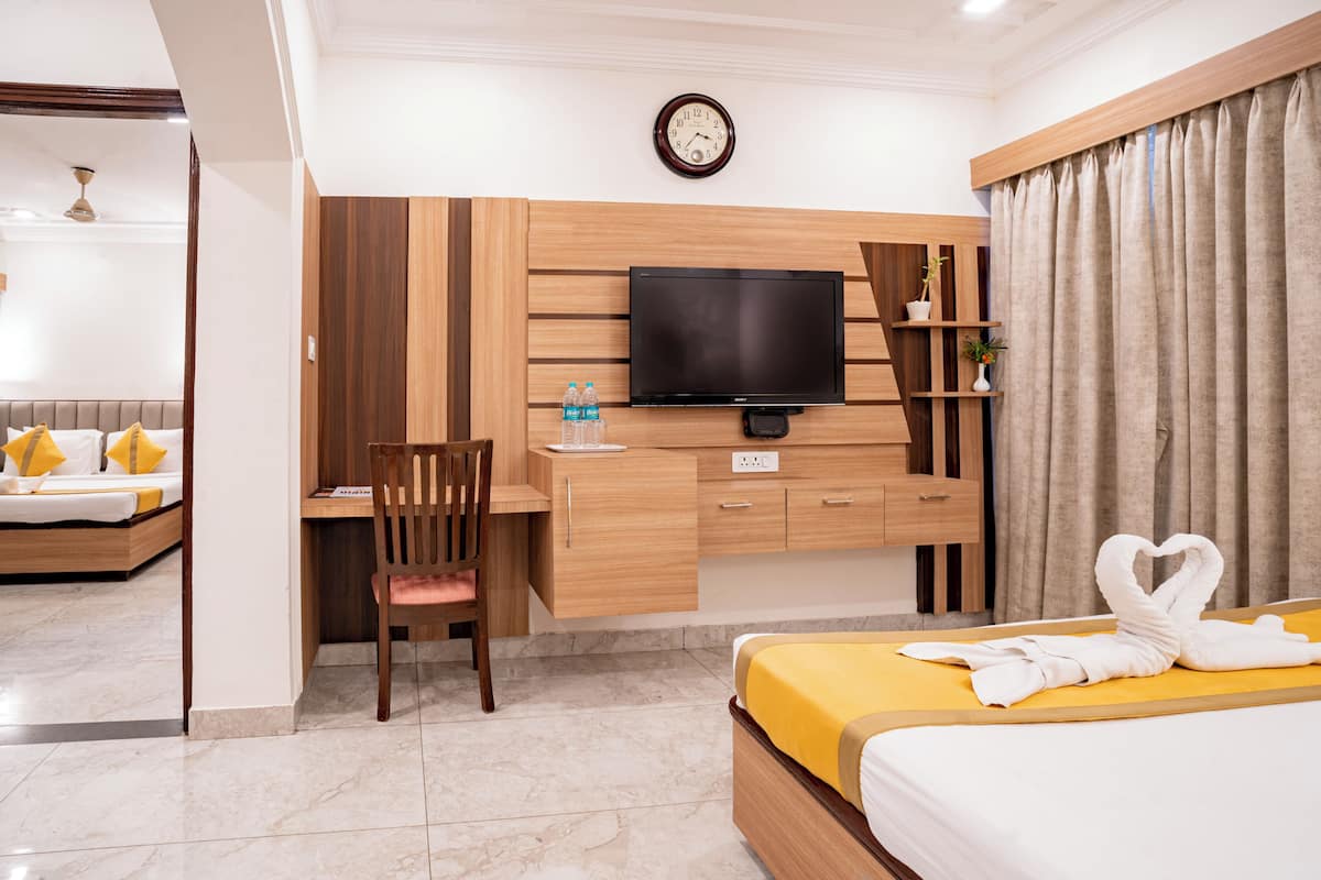 A hotel room with a bed, a desk, a chair, a television, and a clock on the wall.