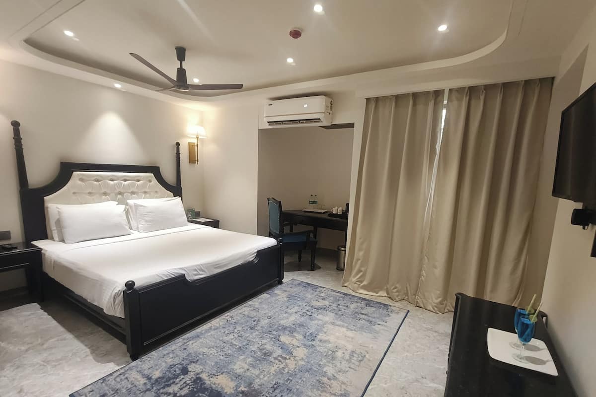 A hotel room with a bed, a desk, a chair, a TV, and an air conditioning unit.