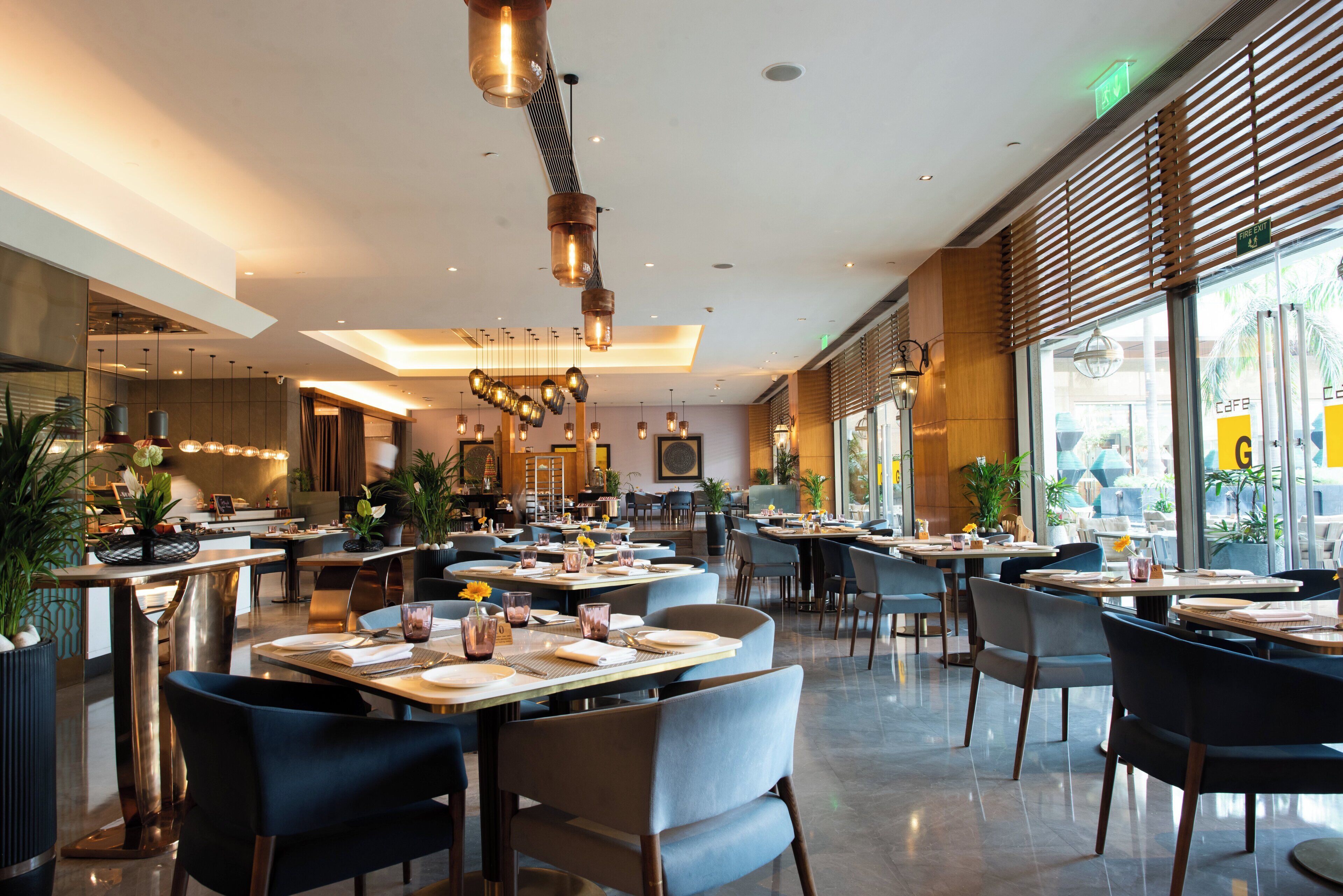 Un restaurante moderno con techos altos, iluminación colgante y diferentes opciones de asientos.