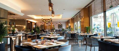 Un restaurante moderno con techos altos, iluminación colgante y diferentes opciones de asientos.