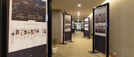 A hallway with informational posters, a potted plant, and a carpeted floor.