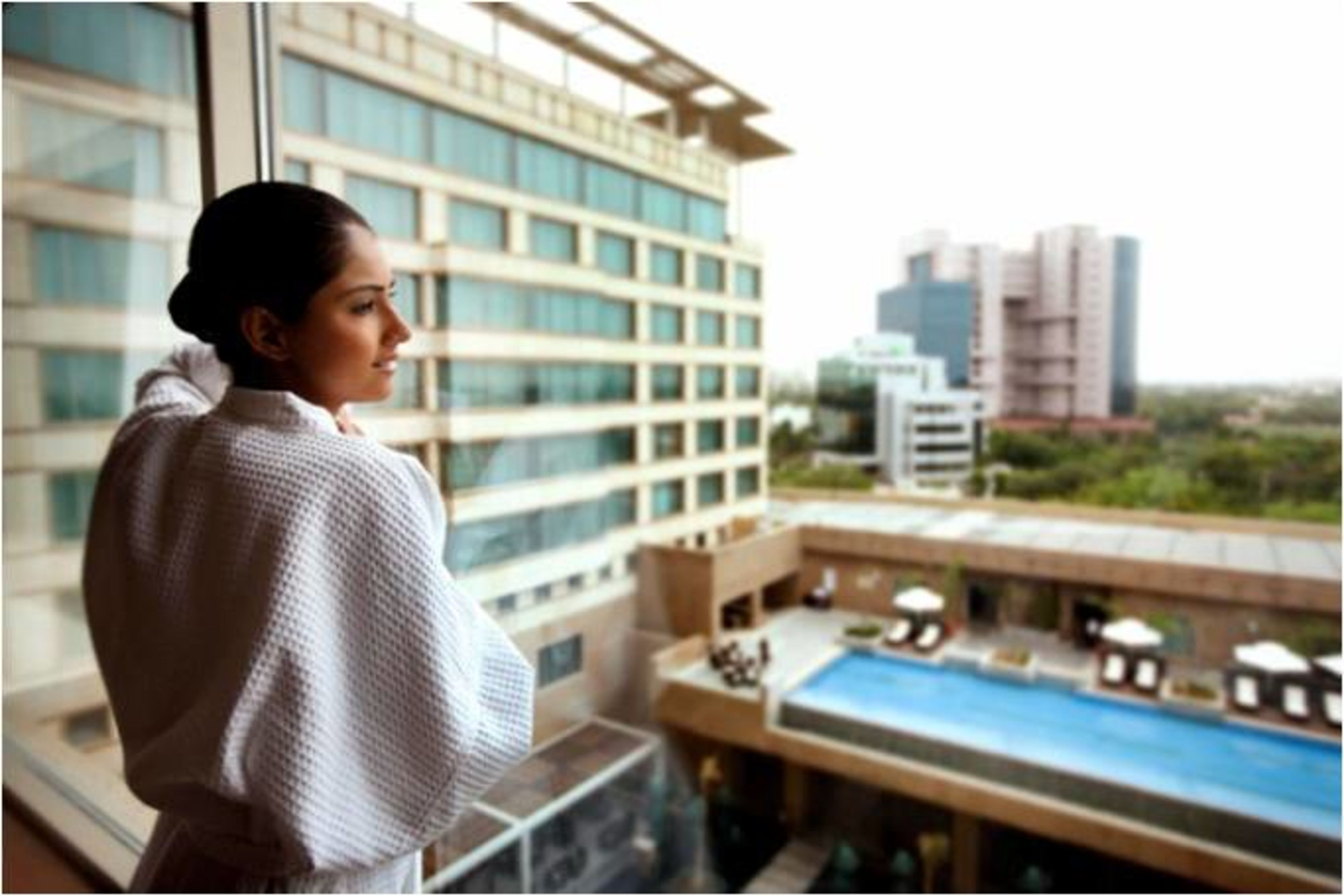A person standing by a window overlooking a pool area with a view of modern buildings.