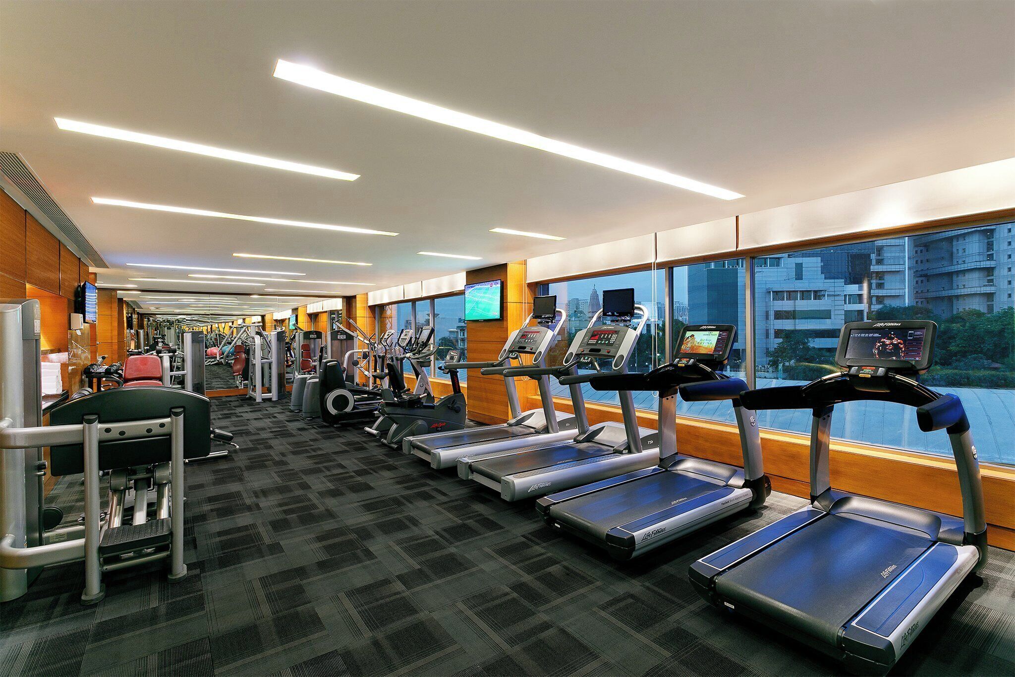A gym with treadmills, weight machines, and a large window with a city view.