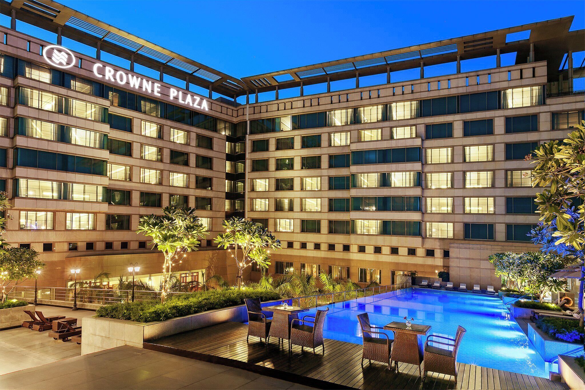 A hotel with a swimming pool, outdoor seating, and a well-lit facade.